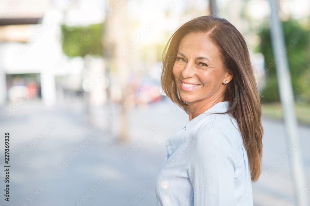 Fototapeta premium Pięknego wieka średniego latynoska kobieta przy miasto ulicą na słonecznym dniu z szczęśliwą twarzy pozycją i ono uśmiecha się z ufnym uśmiechem pokazuje zęby