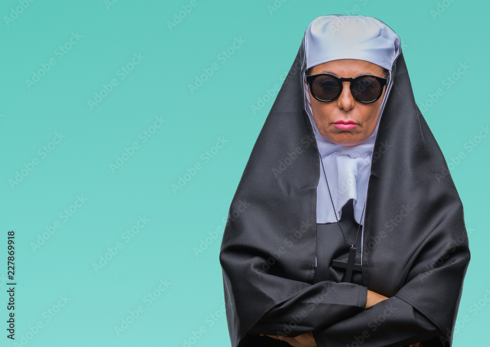 Middle age senior catholic nun woman wearing sunglasses over isolated background skeptic and nervous, disapproving expression on face with crossed arms. Negative person.
