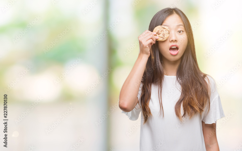 Young asian woman eating chocolate chip cookie over isolated background scared in shock with a surprise face, afraid and excited with fear expression