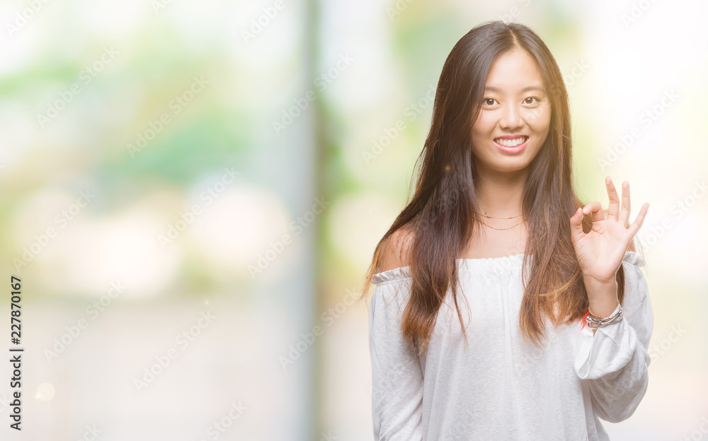 Young asian woman over isolated background smiling positive doing ok sign with hand and fingers. Successful expression.