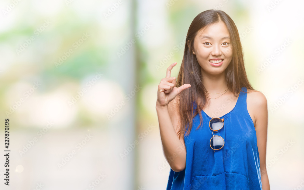 Young asian woman over isolated background smiling and confident gesturing with hand doing size sign with fingers while looking and the camera. Measure concept.