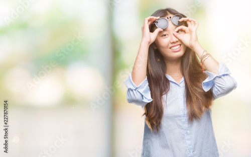 Young asian woman wearing sunglasses over isolated background doing ok gesture with hand smiling, eye looking through fingers with happy face.