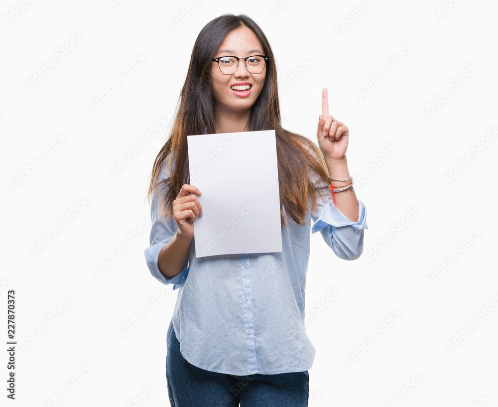 Young asian woman holding blank paper over isolated background surprised with an idea or question pointing finger with happy face, number one Young asian woman holding blank paper over isolated background surprised with an idea or question pointing finger with happy face, number one