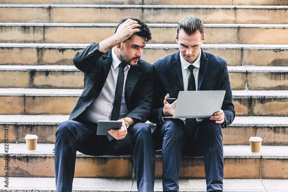 Successful of two businessman in black elegant suit sitting and working with laptop computer on the city.Business and success concept Successful of two businessman in black elegant suit sitting and working with laptop computer on the city.Business and success concept