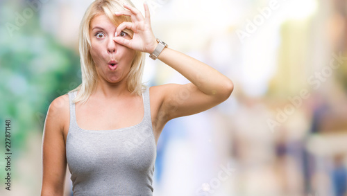 Young beautiful blonde woman over isolated background doing ok gesture shocked with surprised face, eye looking through fingers. Unbelieving expression.