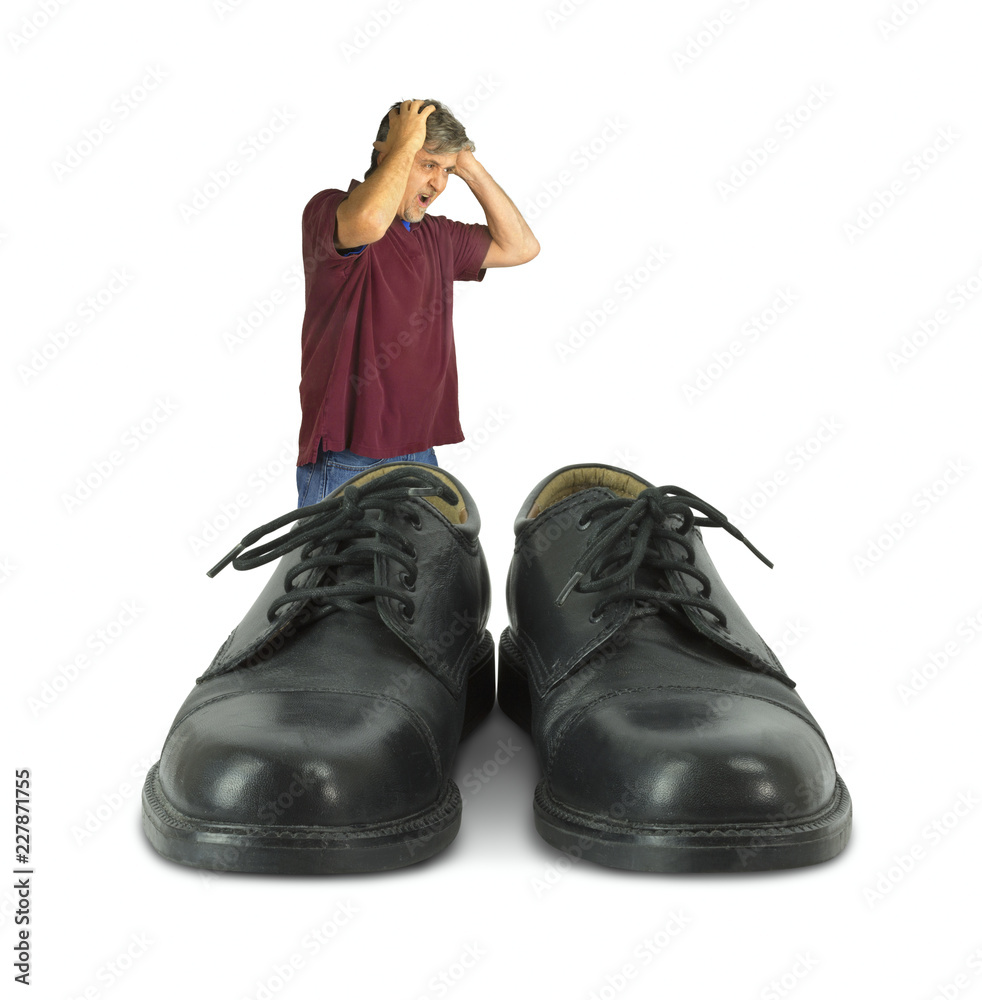 Foto Stock Upset man standing in front of some big shoes to fill  representing huge work challenges when doing someone else's job, goals with  marketing, lack of experience and professional objectives.