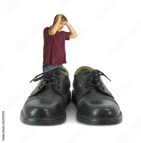 Upset man standing in front of some big shoes to fill representing huge work challenges when doing someone else’s job, goals with marketing, lack of experience and professional objectives.