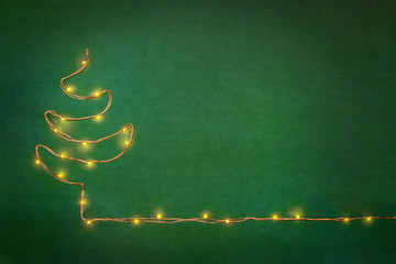 Christmas lights garland arranged like christmas tree over green background. Flat lay, copy space.