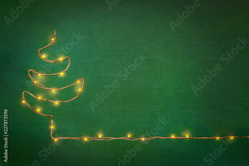 Obraz na płótnie Christmas lights garland arranged like christmas tree over green background. Flat lay, copy space. w salonie