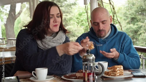 Young couple sitting at a table in a street cafe. They are having fun and feeding each other a cake.