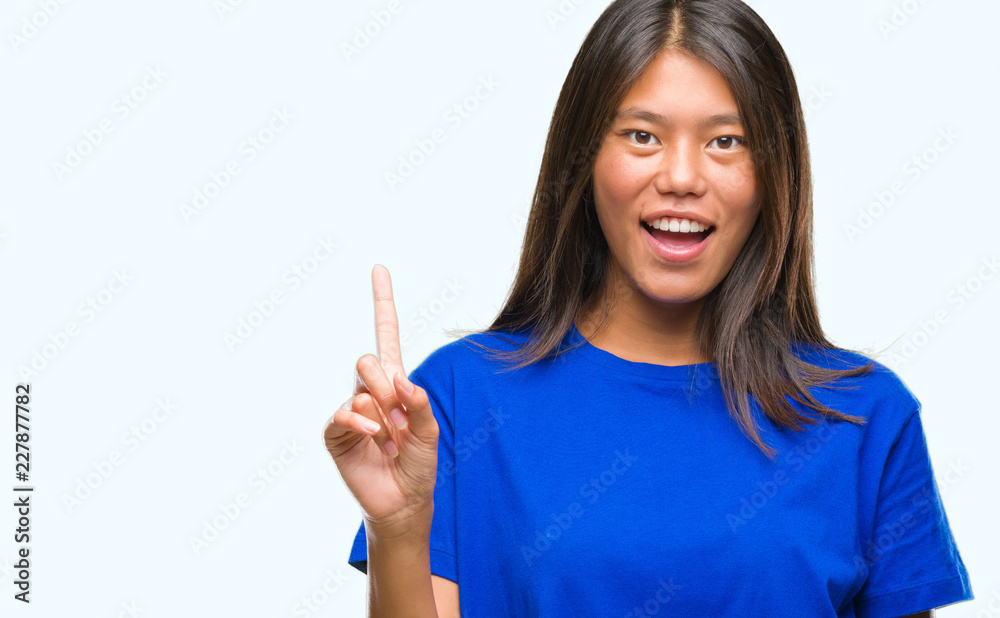 Young asian woman over isolated background showing and pointing up with finger number one while smiling confident and happy. Young asian woman over isolated background showing and pointing up with finger number one while smiling confident and happy.