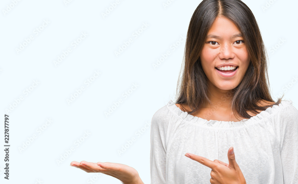 Young asian woman over isolated background amazed and smiling to the camera while presenting with hand and pointing with finger. Young asian woman over isolated background amazed and smiling to the camera while presenting with hand and pointing with finger.