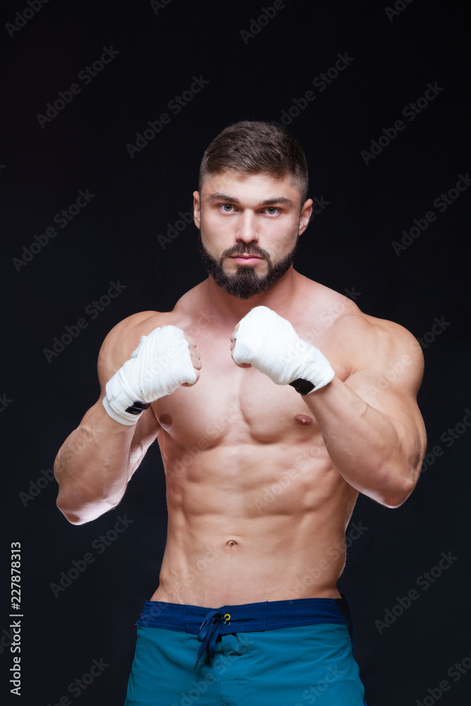 Muscular Fighter kickbox With white Bandages against the black background.
