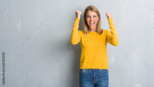 Beautiful young woman standing over grunge grey wall angry and mad raising fist frustrated and furious while shouting with anger. Rage and aggressive concept.