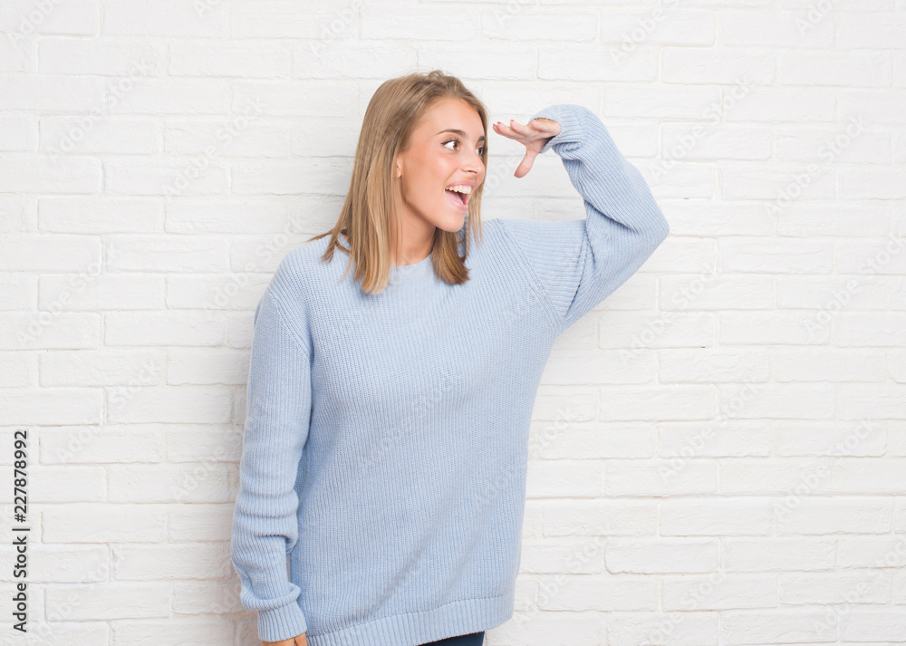 Beautiful young woman over white brick wall very happy and smiling looking far away with hand over head. Searching concept. Beautiful young woman over white brick wall very happy and smiling looking far away with hand over head. Searching concept.
