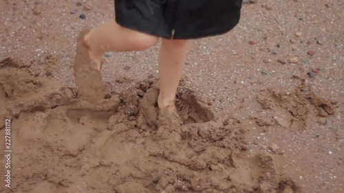 Close up video of the feet of a young boy dancing barefoot in the mud.  He is spinning and wearing a raincoat that is too big and the arms flap as he turns.  Rainy day play.