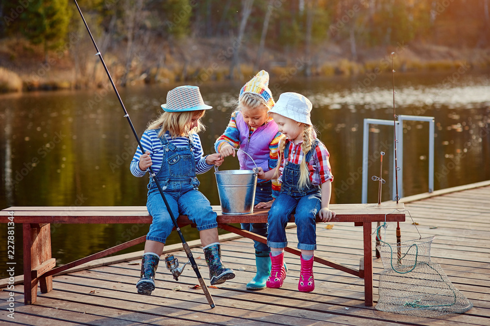 Three little happy girls brag about fish caught on a fishing pole. Fishing from a wooden pontoon. Three little happy girls brag about fish caught on a fishing pole. Fishing from a wooden pontoon.