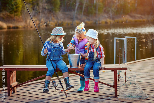 Three little happy girls brag about fish caught on a fishing pole. Fishing from a wooden pontoon.