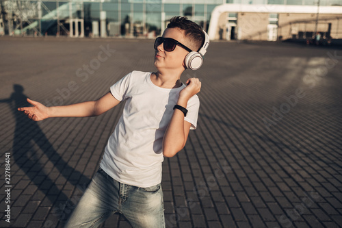 Portrait of a Little Boy in Black Sunglasses and White T-Shirt Listening to Music with Withe Headphones Outdoors