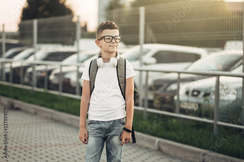 Portrait of a Little Boy in Black Sunglasses and White T-Shirt Listening to Music with Withe Headphones Outdoors