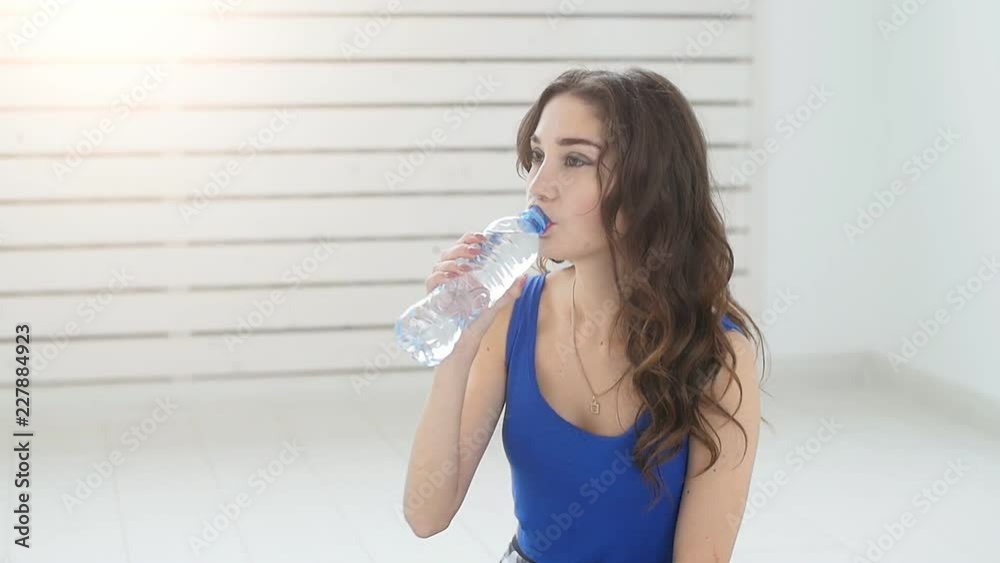 Young woman relaxing after training routine in gym hall, resfreshing herself with drinking water indoors Young woman relaxing after training routine in gym hall, resfreshing herself with drinking water indoors