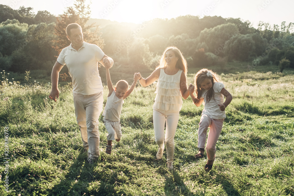 Obraz premium Adult couple with their little children having picnic in the Park Outside the City, Family Weekend Concept, Four People Enjoying Summer Time