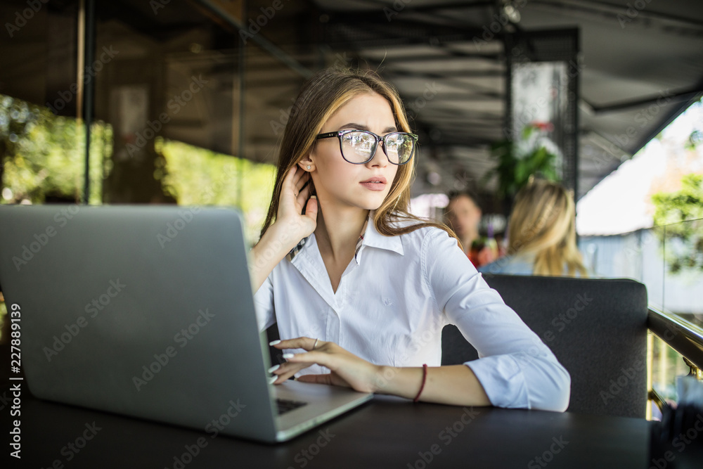 Concentrated at work. Confident young woman in smart casual wear and glasses working on laptop while sitting in creative office or cafe Concentrated at work. Confident young woman in smart casual wear and glasses working on laptop while sitting in creative office or cafe