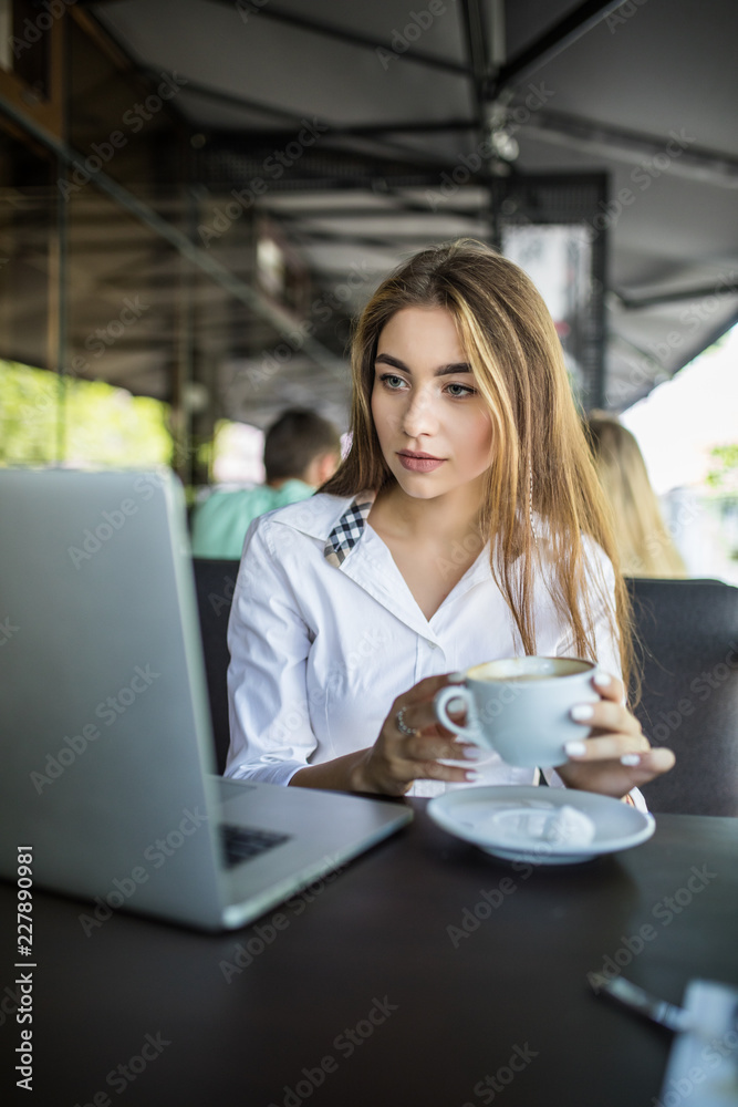 Beautiful hipster woman using laptop drinking coffee at cafe Beautiful hipster woman using laptop drinking coffee at cafe