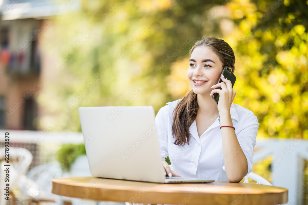 Busy businesswoman talking on mobile phone sitting at the cafe table with laptop Outdoors Busy businesswoman talking on mobile phone sitting at the cafe table with laptop Outdoors