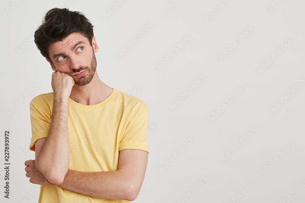 Portrait of bored, propping up his head young man with beard wearing yellow classic tshirt, isolated over white background Portrait of bored, propping up his head young man with beard wearing yellow classic tshirt, isolated over white background