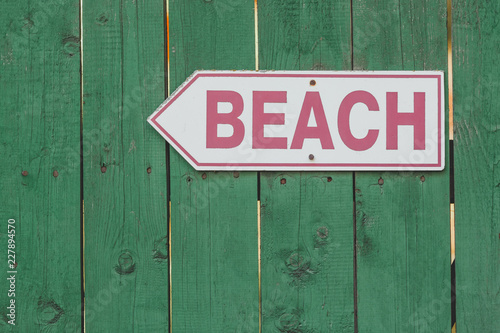Beach access sign on rustic green wooden fence.