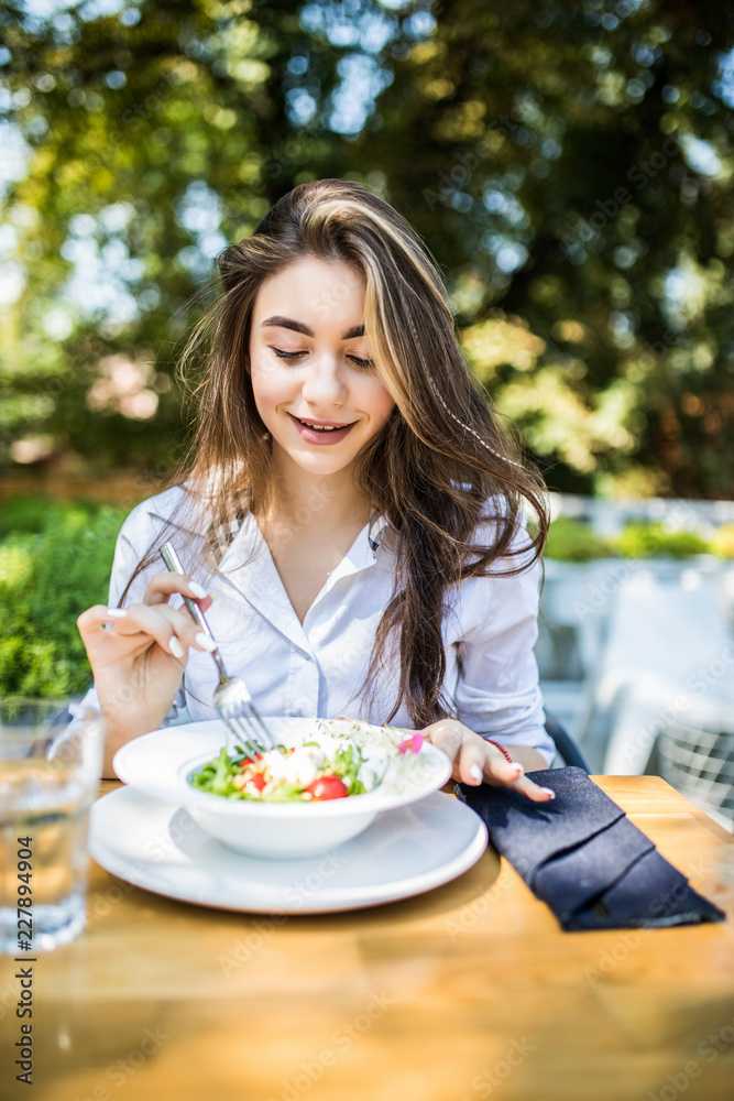 Young woman is eating mixed vegetable salad in cafe outdoors Young woman is eating mixed vegetable salad in cafe outdoors