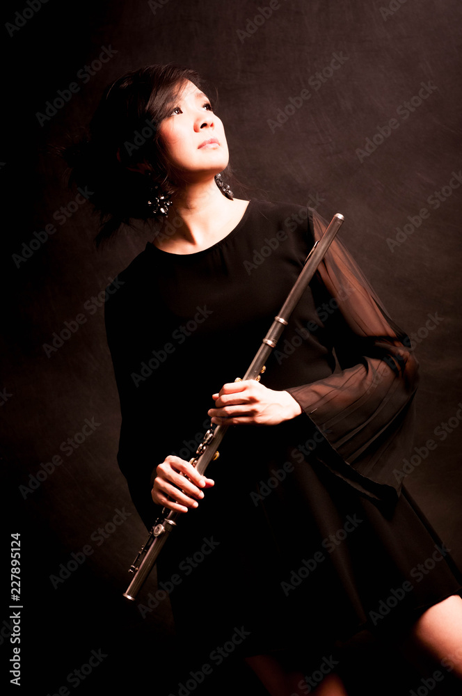 Fashion portrait in studio of beautiful young woman feeling happy with her flute against dark background in studio Fashion portrait in studio of beautiful young woman feeling happy with her flute against dark background in studio