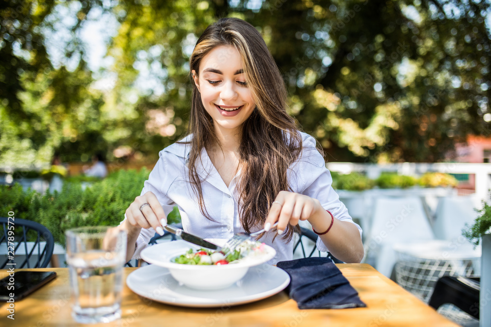 Young woman eating healthy food sitting in the beautiful interior with green flowers on the background in cafe Young woman eating healthy food sitting in the beautiful interior with green flowers on the background in cafe
