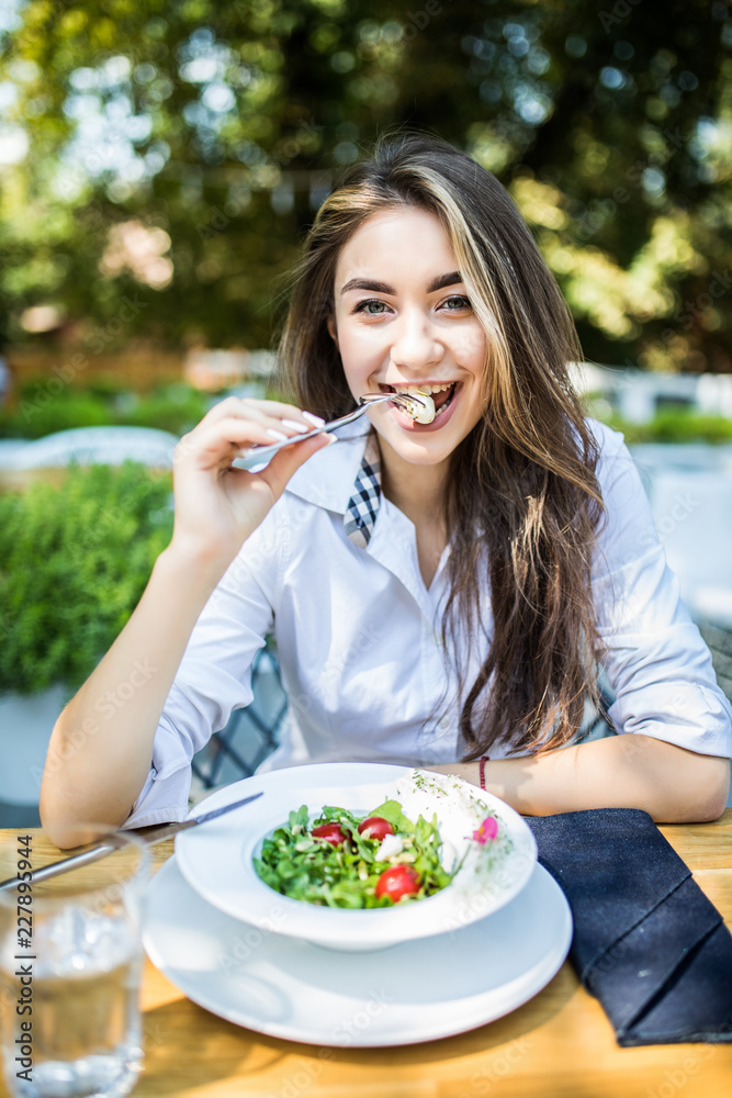 Portrait of young attractive woman eating salad at street cafe.