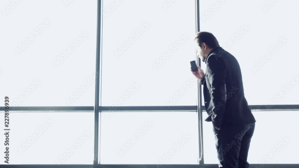 Silhouette businessman on background of large panoramic window. Successful businessman answers an important phone call on smartphone. At the airport. Concept of advertising business in minimal style.