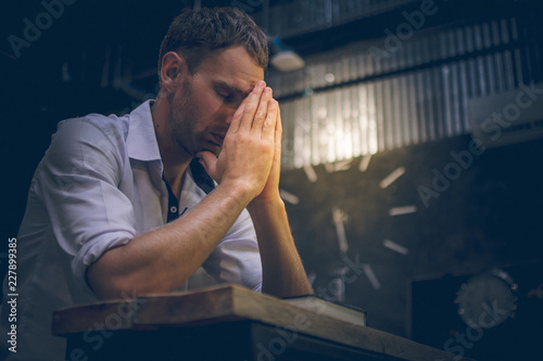 The young man handsome caucasian Americans handsome man sitting with hands clasped in prayer for blessings from God. A Bible rested on a wooden table with copy space.