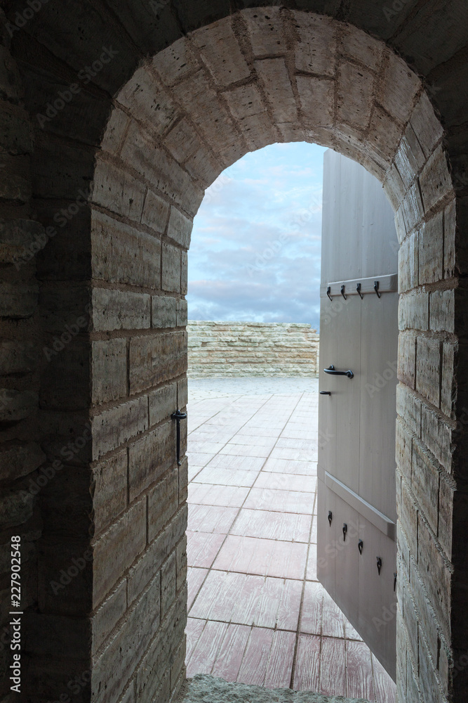 The open door of the old castle through which you can see the blue sky with clouds. Oval arch of the door.