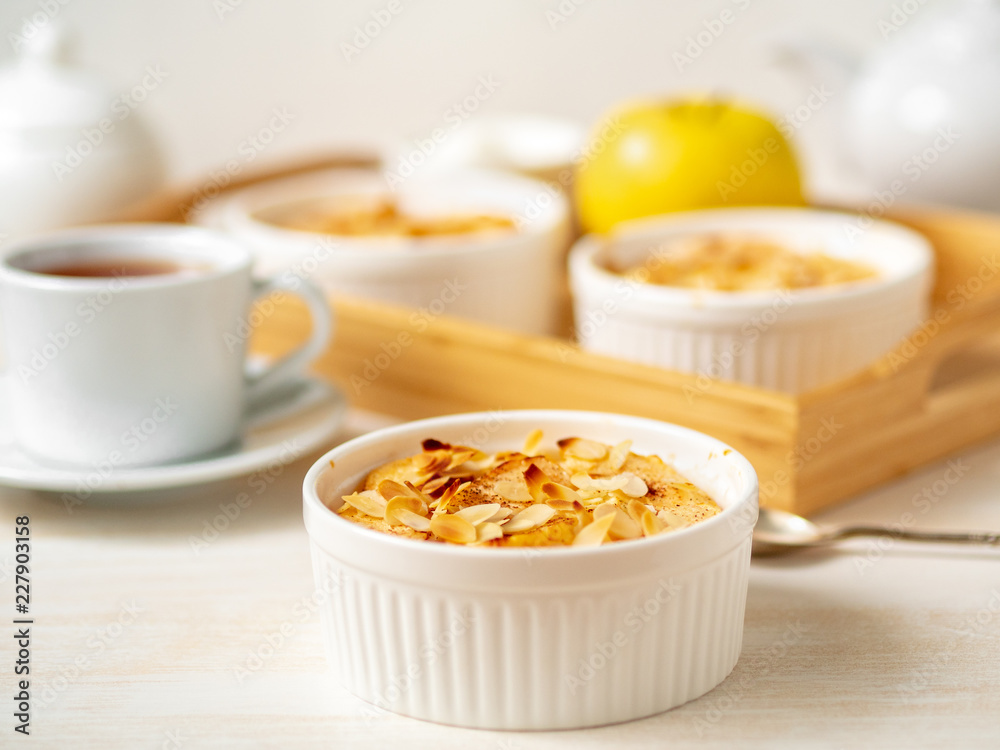 Cheesecake on white wooden table in kitchen. Delicate curd dessert with apples, almond flakes and cinnamon, side view Cheesecake on white wooden table in kitchen. Delicate curd dessert with apples, almond flakes and cinnamon, side view