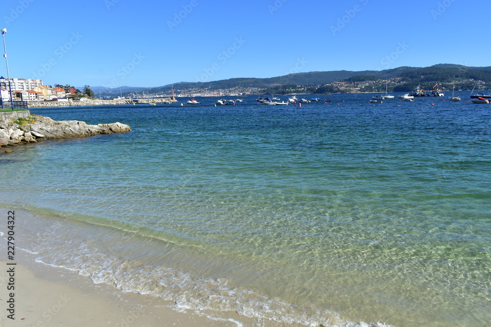 Bay with small coastal village and beach. Clear water with turquoise, green and blue colours. Galicia, Rias Baixas, Spain.