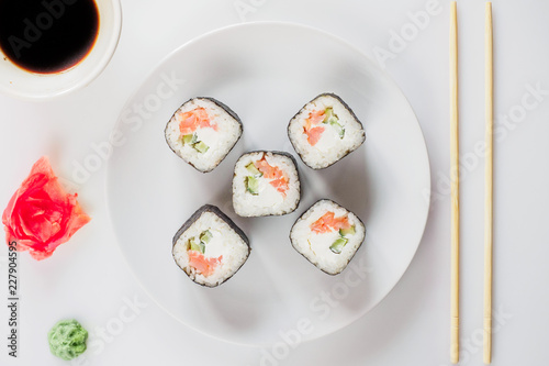 Japanese restaurant, sushi roll on white plate. Set for one person with chopsticks, ginger, soy, top view, copy space