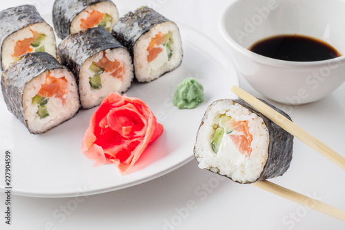 Roll of sushi on a plate, Sushi roll on a tablet on the table restaurant / eating sushi roll using chopsticks, white background, Sushi roll and hand with chopsticks. Japanese food.
