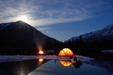 Camp near the mountain lake. Night landscape with a tent near the water.