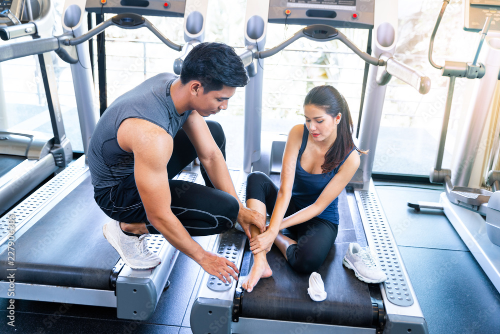 Fototapeta premium professional fitness coach is checking his student who sprained her ankle when running on the treadmill in the gym.