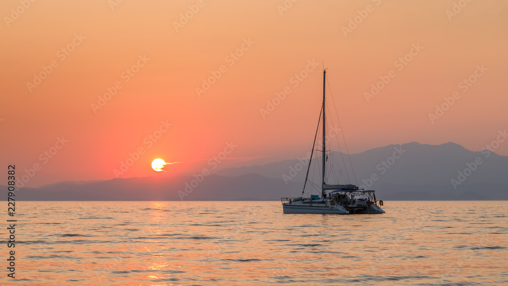 Yacht in the sea at sunset. Beautiful orange sunset colors, mountains in the background. Calm and tranquility. Holidays in Greece.