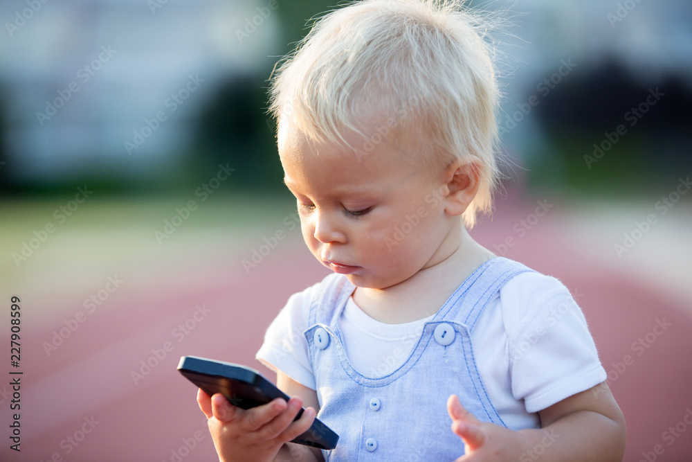 Cute baby boy playing with mobile phone in the park, digital technologies in the hands of a child. Cute baby boy playing with mobile phone in the park, digital technologies in the hands of a child.