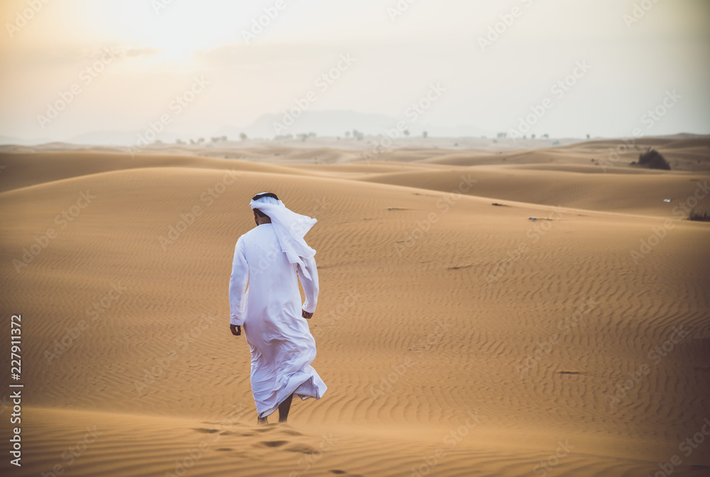 Fototapeta premium Arabski mężczyzna chodzący po pustyni z tradycyjnymi ubraniami emiratów