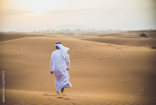 Arabic man with traditional emirates clothes walking in the desert