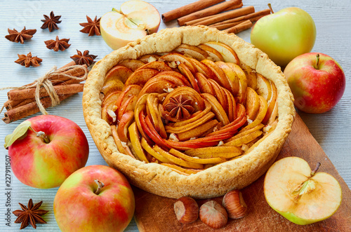 Autumn apple pie on the wooden board decorated with fresh apples, hazelnuts and spices - anise stars and cinnamon on the gray kitchen table. Thanksgiving tart with various ingredients. Side view