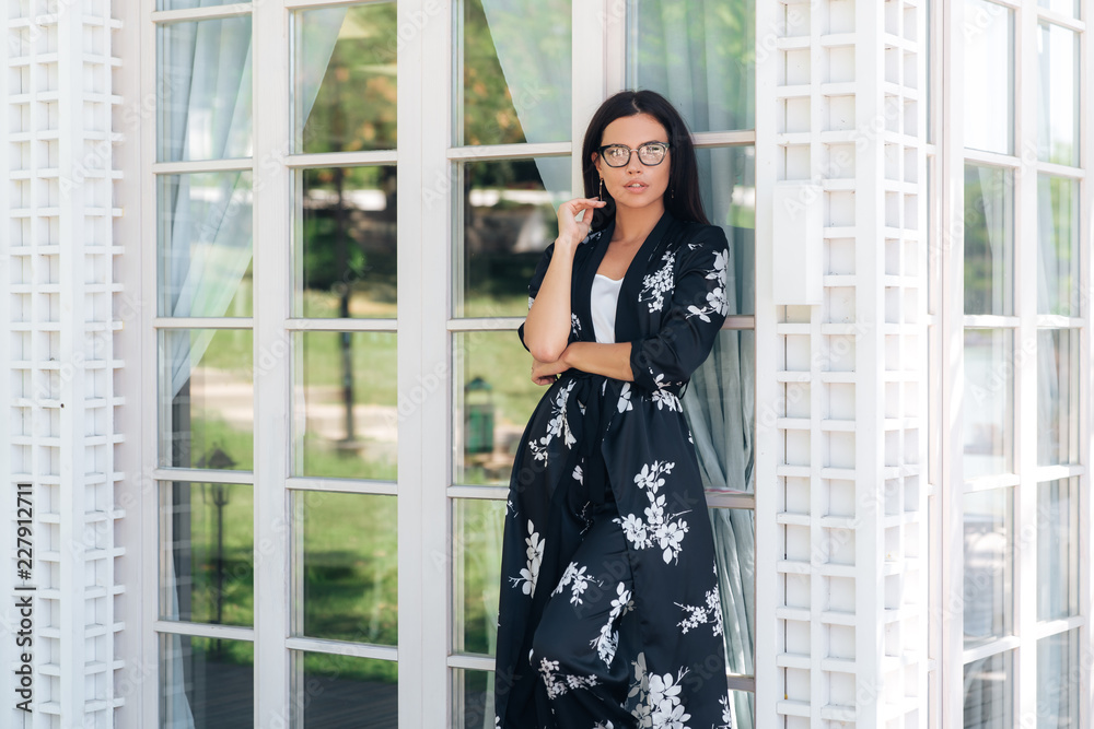 Attractive young woman in silk clothes and fashionable glasses posing against the stained-glass walls of an expensive restaurant. The woman has a European appearance, dark hair, slim figure, stylishly Attractive young woman in silk clothes and fashionable glasses posing against the stained-glass walls of an expensive restaurant. The woman has a European appearance, dark hair, slim figure, stylishly